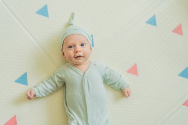 Yeşil şapkalı sevimli bebek oyun hasırının üzerinde yatıyor. Yumuşak dokuları ve parlak renkleriyle yeni doğmuş gibi. Bebek gelişimi, duyusal oyun ve erken çocukluk kavramı..