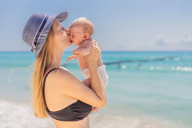 Anne yeni doğmuş bebeğini turkuaz denizde kucaklıyor, huzurlu ve sevgi dolu bir anı paylaşıyor. Aile bağı, annelik ve bebek konseptiyle seyahat..