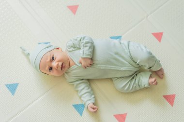 Yeşil şapkalı sevimli bebek oyun hasırının üzerinde yatıyor. Yumuşak dokuları ve parlak renkleriyle yeni doğmuş gibi. Bebek gelişimi, duyusal oyun ve erken çocukluk kavramı..