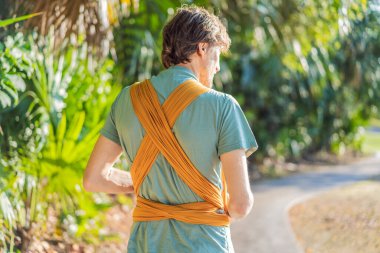 Babam küçük bebeğini parkta sarı bir askıda tutuyor. Sıcak ve sevgi dolu bir aile anı. Bebek giyimi, babalık ve ebeveyn-çocuk bağlama kavramı..