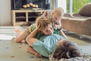 Baba, oğul ve yeni doğan bebek sıcak bir kreşte yerde yatıyorlar ve yeni aile üyelerinin gelişini kutluyorlar. Ebeveynlik, bağlılık ve aile sevgisi kavramı.