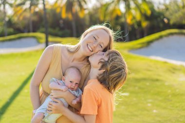 Anne, büyük oğul ve parkta bir çayırda yeni doğmuş bebek. Aile, doğada birlikte kaliteli zaman geçirir. Ebeveynlik, sevgi ve aile bağı kavramı.