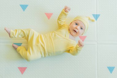Sarı şapkalı sevimli bebek oyun hasırının üzerinde yatıyor. Yumuşak dokuları ve parlak renkleriyle yeni doğmuş gibi. Bebek gelişimi, duyusal oyun ve erken çocukluk kavramı..