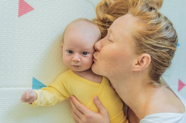 Anne ve bebek oyun hasırının üzerinde yatıyor. Hassas bağ anı, rahat çocukluk atmosferi ve erken gelişim. Ebeveynlik, sevgi ve bebek bakımı konsepti.