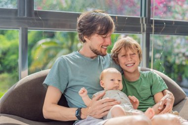 Baba, oğul ve yeni doğan bebek kanepede oturup ailelerine yeni katılan kişiyi neşeyle kutluyorlar. Ebeveynlik, bağlılık ve aile sevgisi kavramı.