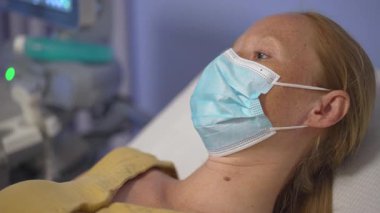 Klinikteki ultrason çekimleri sırasında tıbbi maskeli hamile kadının yakın plan portresi. Doğum öncesi sağlık ve annelik konsepti.