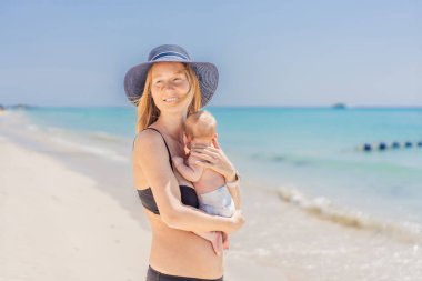 Anne yeni doğmuş bebeğini turkuaz denizde kucaklıyor, huzurlu ve sevgi dolu bir anı paylaşıyor. Aile bağı, annelik ve bebek konseptiyle seyahat..