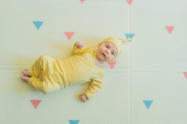 Sarı şapkalı sevimli bebek oyun hasırının üzerinde yatıyor. Yumuşak dokuları ve parlak renkleriyle yeni doğmuş gibi. Bebek gelişimi, duyusal oyun ve erken çocukluk kavramı..