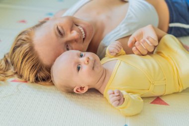 Anne ve bebek oyun hasırının üzerinde yatıyor. Hassas bağ anı, rahat çocukluk atmosferi ve erken gelişim. Ebeveynlik, sevgi ve bebek bakımı konsepti.