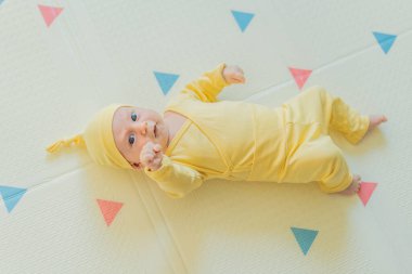 Sarı şapkalı sevimli bebek oyun hasırının üzerinde yatıyor. Yumuşak dokuları ve parlak renkleriyle yeni doğmuş gibi. Bebek gelişimi, duyusal oyun ve erken çocukluk kavramı..
