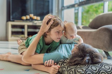 Baba, oğul ve yeni doğan bebek sıcak bir kreşte yerde yatıyorlar ve yeni aile üyelerinin gelişini kutluyorlar. Ebeveynlik, bağlılık ve aile sevgisi kavramı.