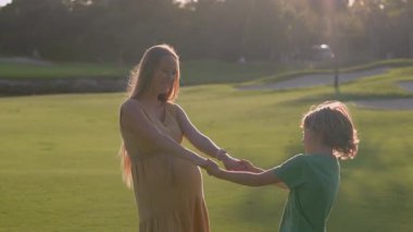 Hamile anne ve büyük oğlu gün batımında yemyeşil bir alanda neşeli anların tadını çıkarıyorlar. Güzel annelik bağı, çocukluk sevinci ve sevgi dolu aile zamanı. Açık havada mutluluk