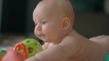 3 aylık bir erkek bebek yerde yatar ve oyuncaklarla oynar. Erken gelişim sırasında karın ve duyusal keşiflerin tadını çıkarır..