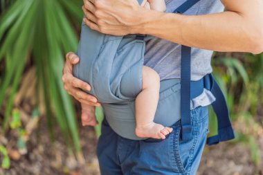 Genç bir baba, bebeğiyle birlikte doğada ebeveynlere bakan ergonomik bir bebek taşıyıcısının içinde dolaşıyor. Barışçıl bir ortamda bağlılık, sıcaklık ve modern ebeveynlik kavramı.