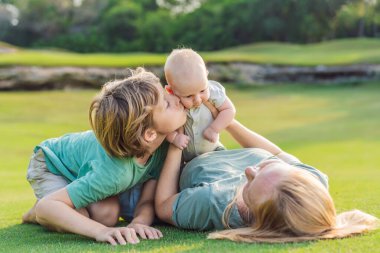 Anne, büyük oğul ve parkta bir çayırda yeni doğmuş bebek. Aile, doğada birlikte kaliteli zaman geçirir. Ebeveynlik, sevgi ve aile bağı kavramı.