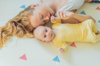 Anne ve bebek oyun hasırının üzerinde yatıyor. Hassas bağ anı, rahat çocukluk atmosferi ve erken gelişim. Ebeveynlik, sevgi ve bebek bakımı konsepti.