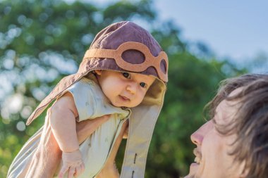 Baba pilot şapkasıyla bebeği kaldırıyor. Geleceğin pilot rüyası, havacılık ilhamı ve neşeli aile bağları. Gökyüzü sınırdır..