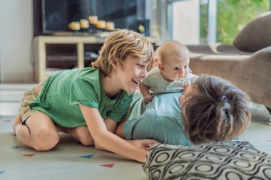 Baba, oğul ve yeni doğan bebek sıcak bir kreşte yerde yatıyorlar ve yeni aile üyelerinin gelişini kutluyorlar. Ebeveynlik, bağlılık ve aile sevgisi kavramı.