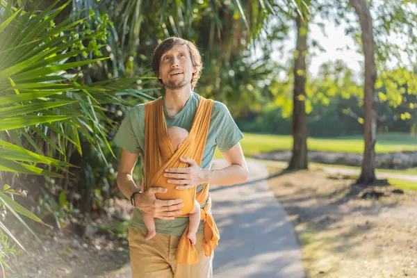 Babam küçük bebeğini parkta sarı bir askıda tutuyor. Sıcak ve sevgi dolu bir aile anı. Bebek giyimi, babalık ve ebeveyn-çocuk bağlama kavramı..