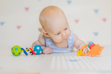 Evdeki yumuşak bir bebek minderinde renkli çıngıraklarla oynayan sevimli bir bebek. Erken gelişim kavramı, duyusal oyun ve bebekler için güvenli öğrenme ortamı.