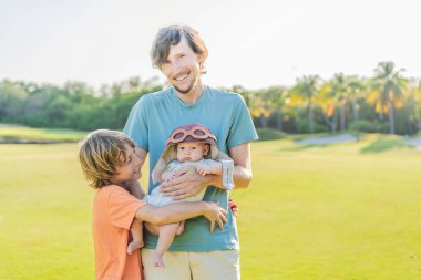 Baba, oğul ve çayır üzerinde yeni doğmuş bir bebek. Pilot şapkası takan bebek havacılık hayallerini sembolize ediyor. Aile bağı kavramı, geleceğin pilotu ve çocukluk arzusu..