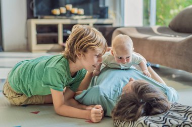 Baba, oğul ve yeni doğan bebek sıcak bir kreşte yerde yatıyorlar ve yeni aile üyelerinin gelişini kutluyorlar. Ebeveynlik, bağlılık ve aile sevgisi kavramı.