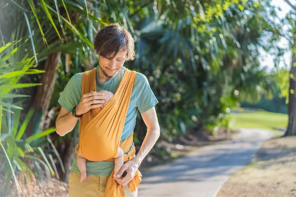 Babam küçük bebeğini parkta sarı bir askıda tutuyor. Sıcak ve sevgi dolu bir aile anı. Bebek giyimi, babalık ve ebeveyn-çocuk bağlama kavramı..