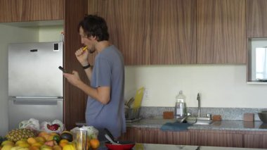 Mutfakta dişlerini fırçalarken telefonunu kullanan genç bir adam, birden fazla iş yapmanın ve telefon bağımlılığının modern bir karışımını sergiliyor. Teknolojinin günlük hayattaki rolünü yansıtan bir an.