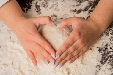 Aşkla yemek pişirmek. Kalp şeklinde hamur tutan kadın elleri. Eller hamura nazikçe kalp şeklinde dokunur. Kalp şeklinde hamur tutan kadın elleri