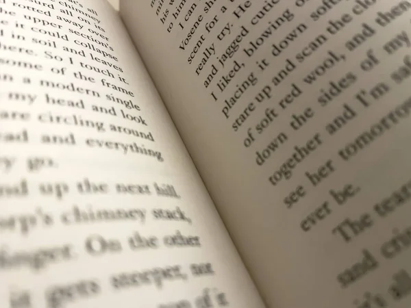 A close up of a book open to two pages with text on either side. The text is in English, some blurred, some in focus. Black text on white page and on an angle.