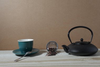 Bir fincan çay, çaydanlık ve ahşap masada yeşil yaprak.