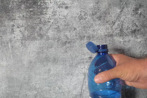 Mavi tişörtlü bir adam gri plastik şişeli boş bir şişe tutuyor..