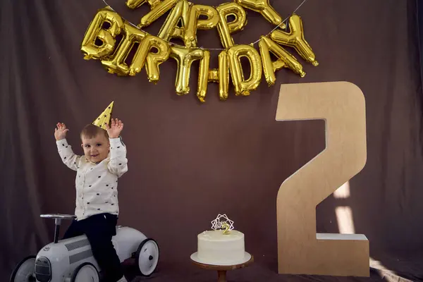 A toddler is happy with a birthday cake and presents on his second birthday