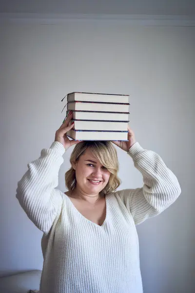 medium-sized woman in light clothes plays with books in a light room