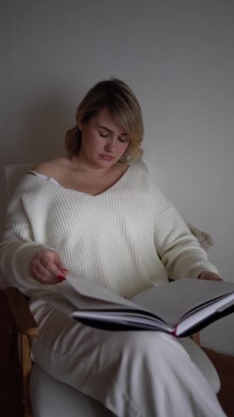Średniej Wielkości Kobieta Jasnych Ubraniach Czyta Książkę Siedząc Białym Krześle — Wideo stockowe