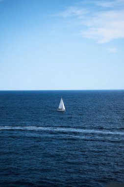        Derin mavi su ve açık mavi gökyüzü ile çevrili yalnız beyaz yelkenli.                    