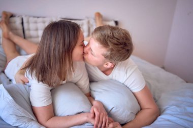 Genç ve güzel bir çift yatakta sarılıp öpüşüyor, evde sağlıkları yerinde.                     