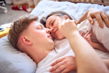                 Genç çift yatakta yatıyor, kız oğlanın omzunda, şefkatle sarılıyor.            