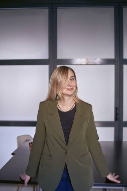 Sarı saçlı, yeşil ceketli ve kot pantolonlu bir kadın.                