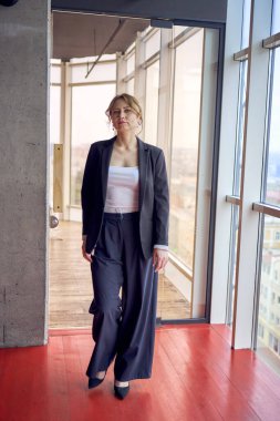 Ben ceketli, beyaz tişörtlü, modern ofiste panoramik pencereli çekici orta yaşlı bir kadınım.                     