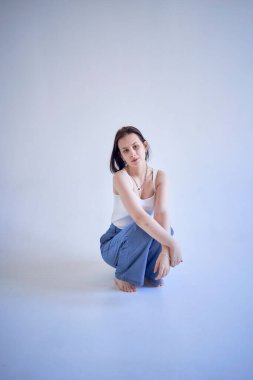 Genç bir kız stüdyoda beyaz bir siklonamada oturuyor.                      