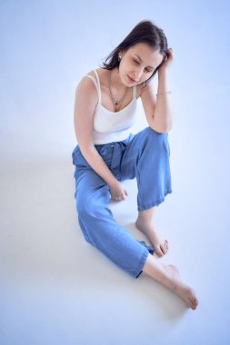 a young teenage girl sits on a white cyclorama in the studio                       clipart