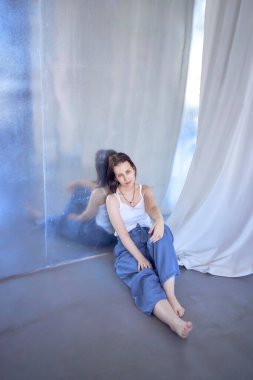 a young teenage girl fighting brain cancer at photo shoot in studio sitting on floor, leaning against metal wall, reflection clipart