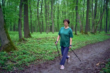 Yaşlı bir kadın İskandinavya 'da Bahar Ormanı' nda sopalarla yürüyor.