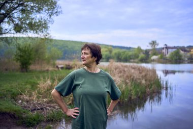 Nehir kıyısında egzersiz yapan yaşlı bir kadın, yanında bir bisiklet ve yoğurt.