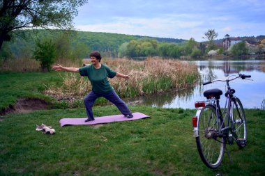 Nehir kıyısında yoga yapan yaşlı bir kadın, evden bisikletle gelmiş.