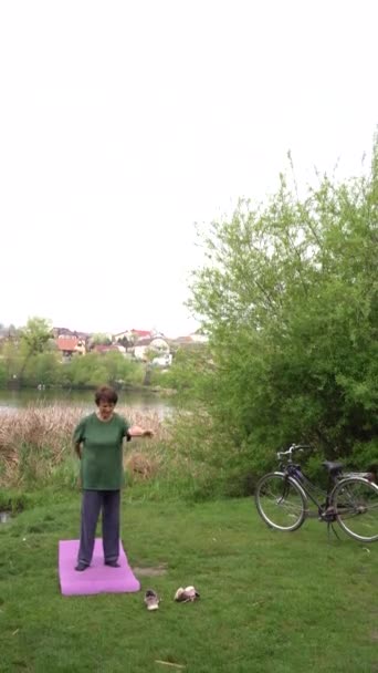 Gammal Kvinna Gör Övningar Morgonen Floden Stranden Cykel Och Yoghamat — Stockvideo