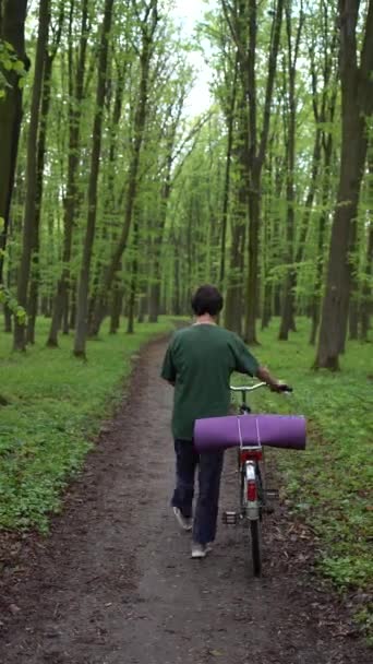 一个骑自行车和瑜伽垫在春天森林里散步的老妇人 — 图库视频影像