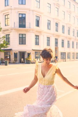 Kopenhag 'ın güneşli sokaklarında kısa saçlı, sarı elbiseli bir kız.