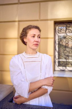 Tiyatronun yanında antika sütunları olan, beyaz, klasik, zarif bir orta yaşlı kadın.